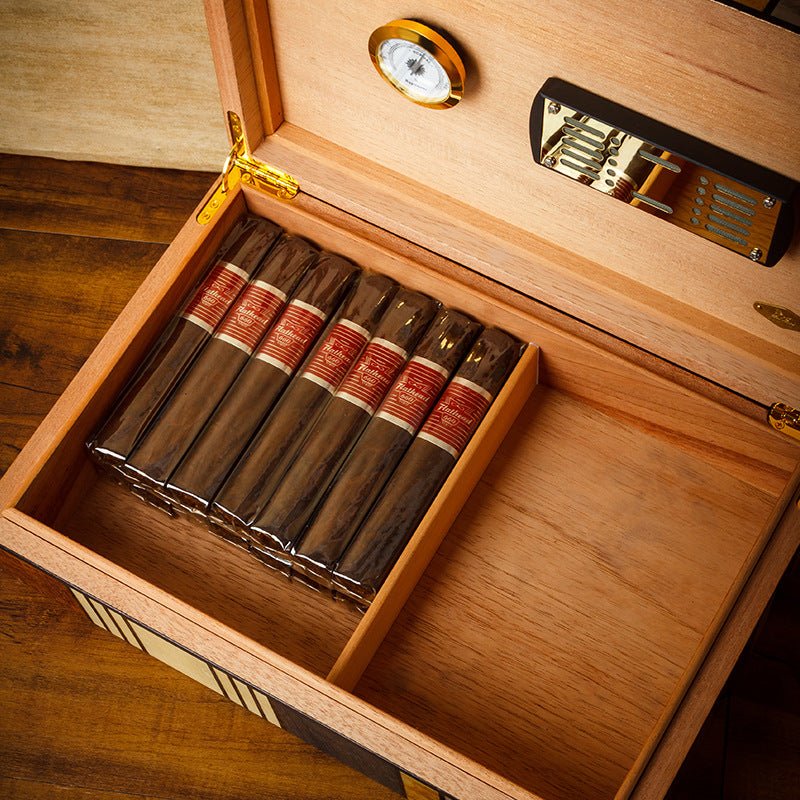 Humidor cigare ouvert sur une table en bois avec six cigares alignés, hygromètre doré et humidificateur visibles