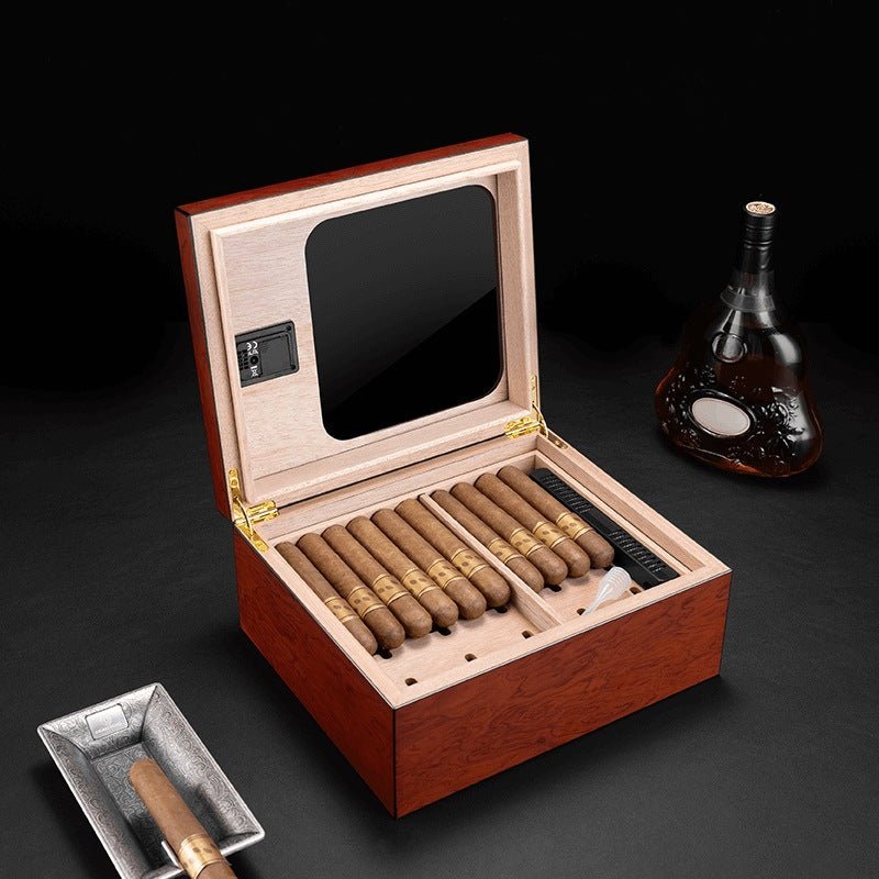 Cave à cigares ouverte montrant plusieurs vitoles de cigare alignées, bouteille de cognac en arrière-plan et petit cendrier avec cigare allumé