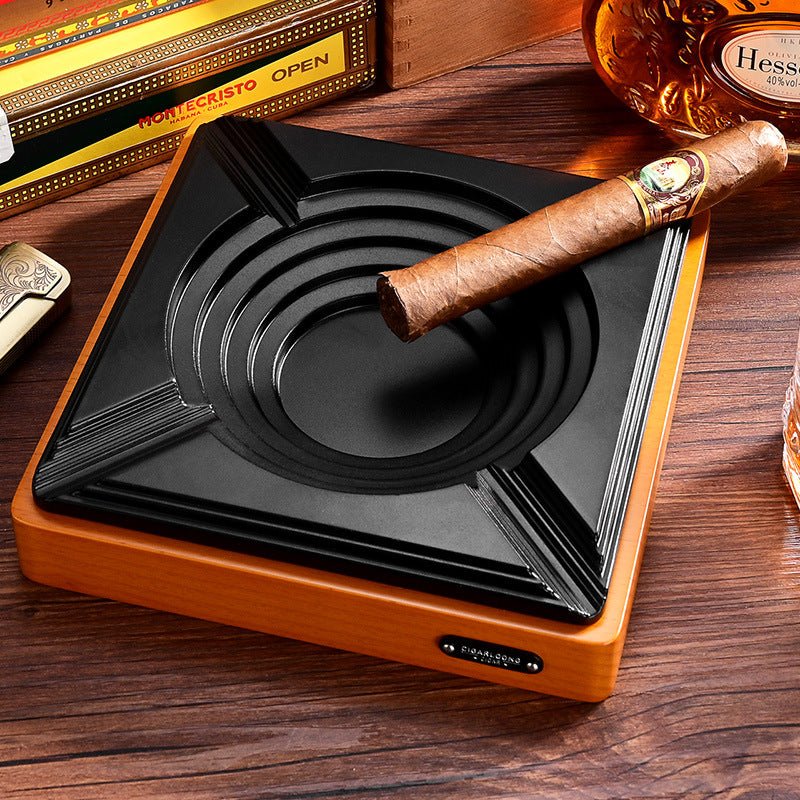 Grandes marques de cigares sur table de bar en bois, cendrier avec cigare posé, boîte Montecristo ouverte, bouteille de cognac Hennessy et coupe-cigare dans une ambiance tamisée