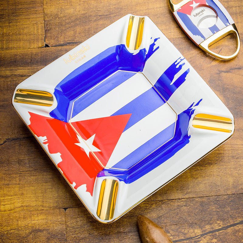 Cigare et whisky, cendrier en céramique aux couleurs cubaines, coupe-cigare en laiton et cigare posés sur une table en bois ambré dans une scène de dégustation lounge