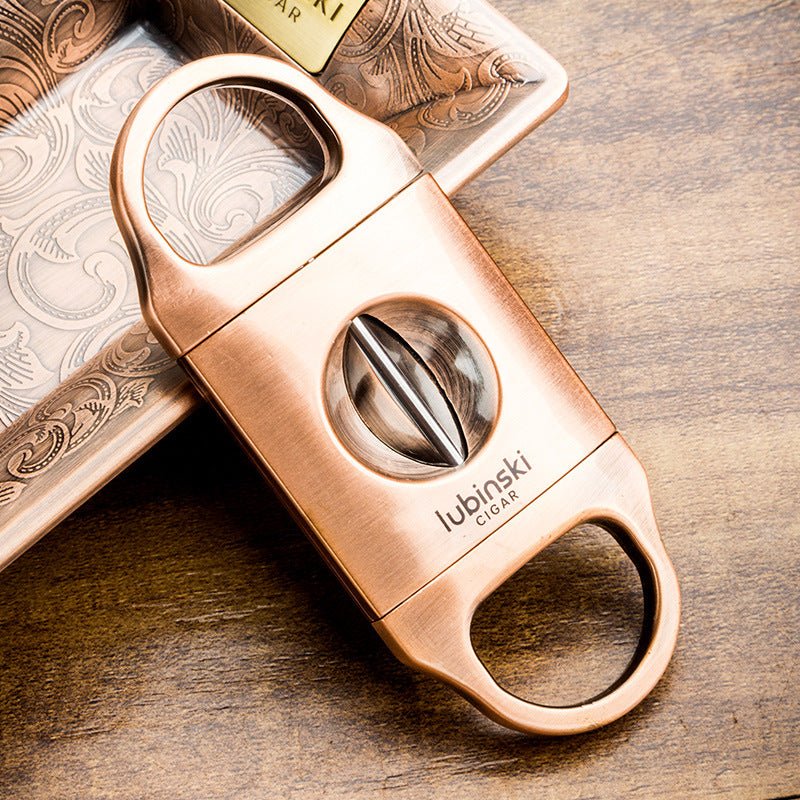 Coupe-cigare en V finition bronze posé sur un cendrier gravé et une table en bois patiné